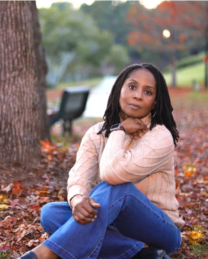 Girl sitting on ground in the fall leaves wearing jeans, and pink sweater.